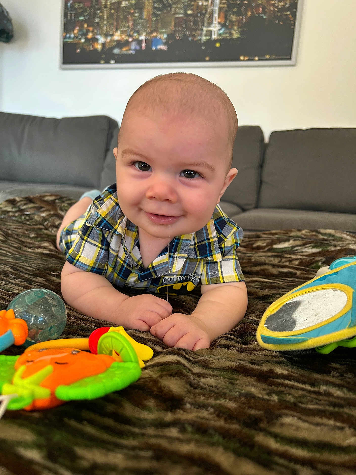 Archer is registered to the contest to win money with this photo: baby, child, smile, plaid_shirt, toy, blanket, couch, indoor, portrait, cute, playtime, infant, happy, face, person, furniture, home, closeup, lying_down, colorful