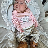 Ailany is registered to the contest to win money with this photo: baby, infant, child, pink_clothing, headband, bow, baby_shoes, patterned_clothing, baby_seat, indoor, face, person, cute, serious_expression, sitting, soft_toys_pattern, footwear, headwear, apparel, newborn