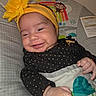 Ailany is registered to the contest to win money with this photo: baby, smiling, headband, yellow_flower, infant, baby_seat, monkey_design, rainbow, black_clothing, gold_dots, hand, face, cheeky_smile, indoor, cozy, child, cute, patterned_fabric, happy, portrait