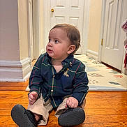 Bruno joined the competition — help win amazing prizes! baby, child, sitting, floor, wooden_floor, shirt, plaid, pants, shoe, indoor, hallway, door, curious, person, young_child, casual_clothing, footwear, home, portrait, looking_away