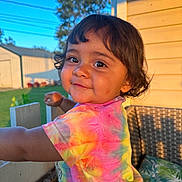 Ann Michelle Reyes is registered to the contest to win money with this photo: child, toddler, girl, portrait, smiling, face, eyes, hair, outdoor, backyard, patio, sunlight, sunset, colorful, tie_dye, shirt, chair, cushion, garden, house