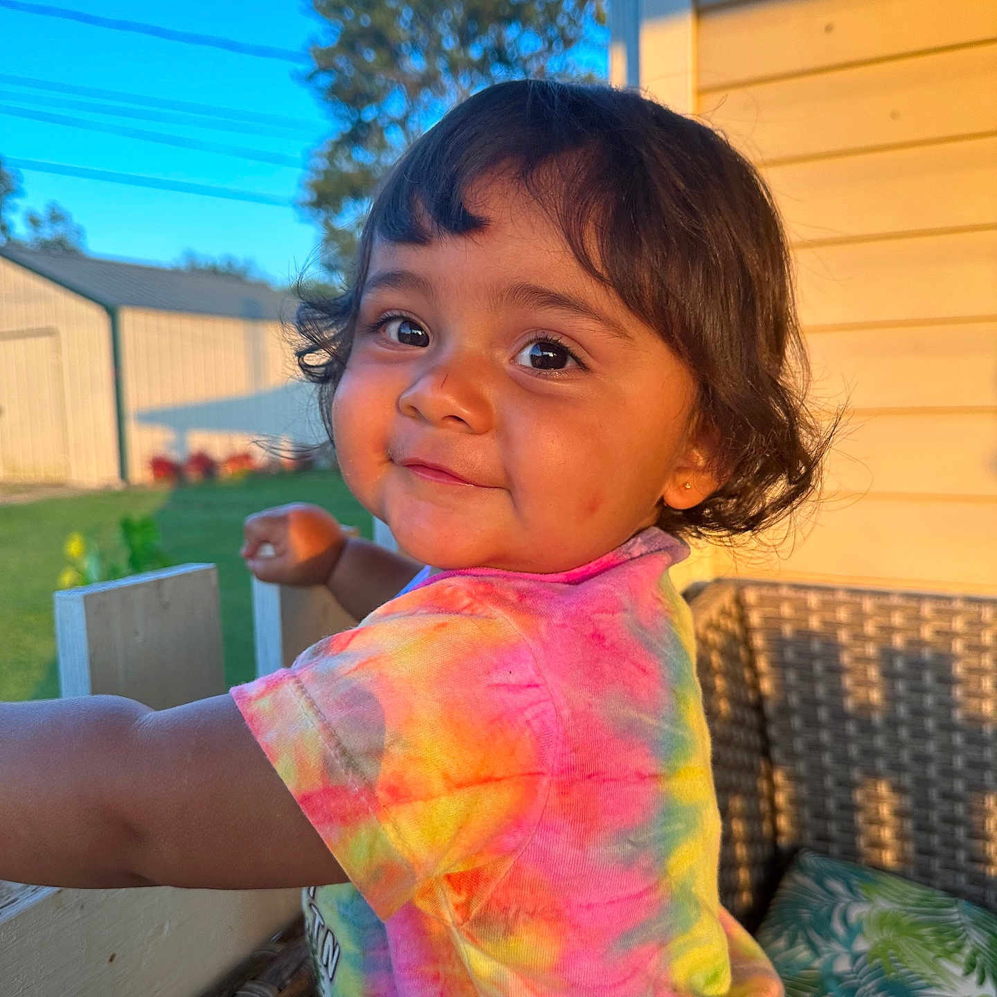 Ann Michelle Reyes is registered to the contest to win money with this photo: child, toddler, girl, portrait, smiling, face, eyes, hair, outdoor, backyard, patio, sunlight, sunset, colorful, tie_dye, shirt, chair, cushion, garden, house