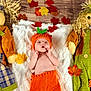 Boston is registered to the contest to win money with this photo: baby, pumpkin_hat, knitwear, scarecrow, doll, autumn_leaves, blanket, fall_theme, orange, green, plush_toy, child, cute, indoor, wood_floor, decor, seasonal, soft_texture, portrait, holiday