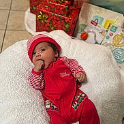 Liam is registered to the contest to win money with this photo: baby, blanket, celebration, child, christmas, cute, decorations, festive, gift_boxes, happy, holiday, holiday_season, indoor, infant, lying_down, person, red_clothing, striped_hat, striped_sleeves, toddler