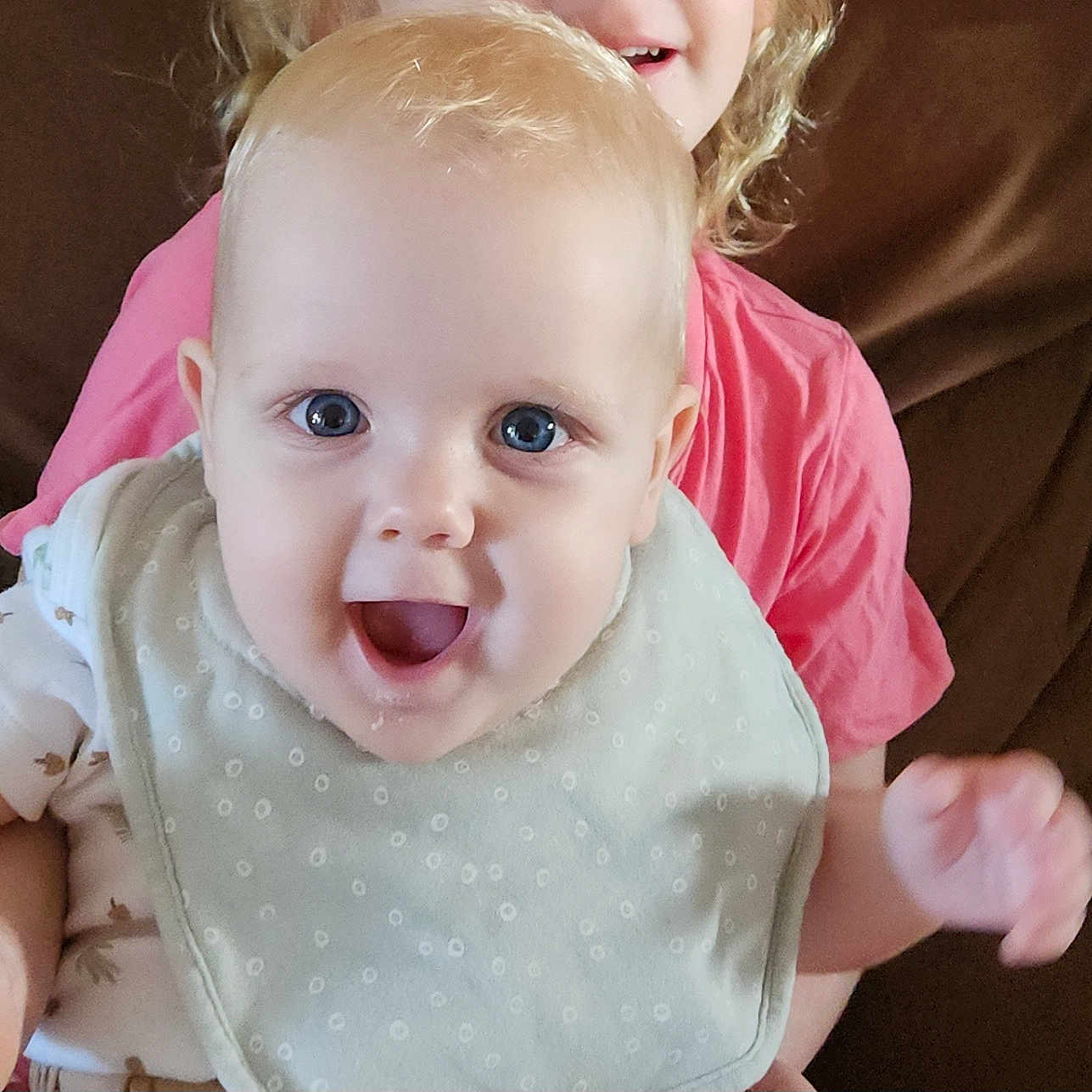 Teejay is registered to the contest to win money with this photo: baby, background, bib, blue_eyes, child, closeup, couch, cute, expression, face, happy, holding, indoor, infant, joyful, light, person, pink_shirt, sitting, smiling