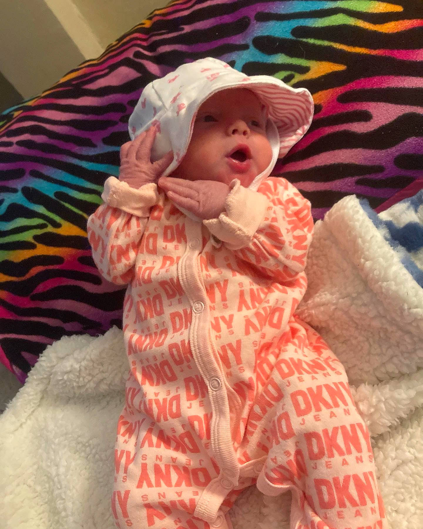 Esme is registered to the contest to win money with this photo: baby, baby_toddler_clothing, cap, cheek, child, comfort, eye, face, fur, hat, headwear, linens, pattern, person, pink, room, sitting, skin, sleeve, sun_hat