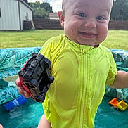 Kohen joined the competition — help win amazing prizes! toddler, child, toy_car, yellow_swimsuit, water, pool, outdoor, grass, backyard, smile, happy, summer, sunlight, water_droplets, face, person, playing, plastic_pool, fun, daylight