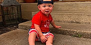 Kohen is registered to the contest to win money with this photo: toddler, child, baby, sitting, porch, concrete, cap, backwards_cap, shorts, red_shirt, barefoot, blue_eyes, potted_plants, lantern, outdoor, summer, curious, smiling, face, person