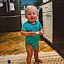 Kohen is registered to the contest to win money with this photo: toddler, child, baby, standing, kitchen, rug, floor, smiling, blue_onesie, barefoot, cabinet, refrigerator, toy, household, indoor, person, happy, home, blonde_hair, small_object