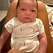 Kaëlya participe au concours pour gagner de l'argent avec cette photo : arm, baby, background, bed, clothing, expression, eyes, fabric, face, furniture, hand, holding, human, indoor, infant, onesie, person, room, sitting, skin