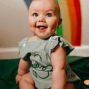 Alora joined the competition — help win amazing prizes! baby, infant, smiling, blue_eyes, dimples, green_outfit, rainbow, portrait, indoor, soft_lighting, sitting, blanket, cheeks, hands, legs, face, skin, button, happy, cute