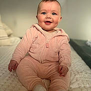 Alora is registered to the contest to win money with this photo: baby, infant, child, smiling, blue_eyes, pink_outfit, hoodie, onesie, sitting, bed, blanket, cozy, cute, portrait, cheeks, hands, feet, toes, indoor, soft_texture
