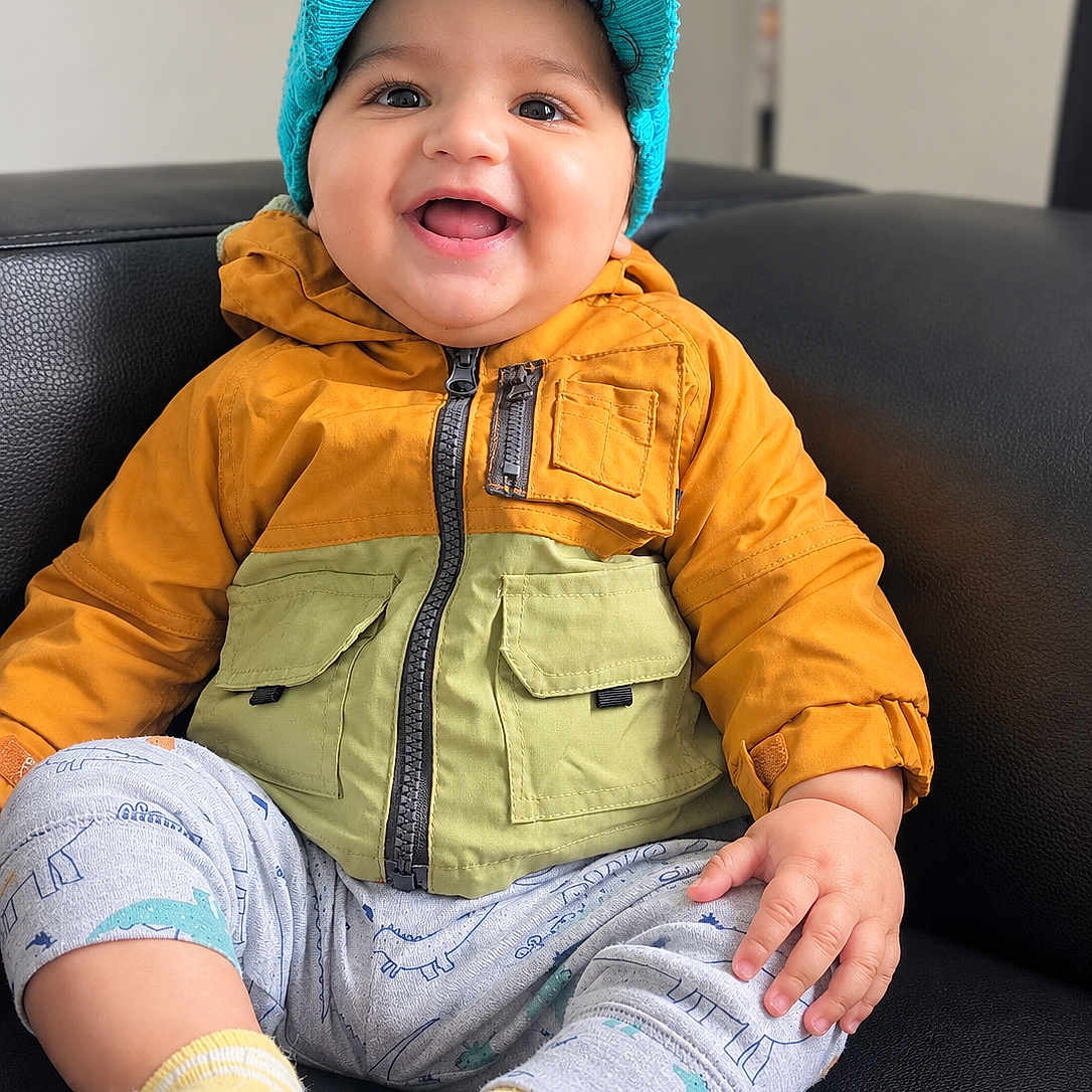 Gurbaaz joined the competition — help win amazing prizes! baby, cap, child, closeup, clothing, couch, face, green, happy, hat, indoor, infant, jacket, orange, photography, portrait, sitting, smiling, socks, yellow