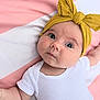 baby, infant, headband, yellow, white_onesie, blanket, pink, white, face, cute, child, laying_down, portrait, soft_texture, newborn, expression, skin, clothing, indoors, closeup