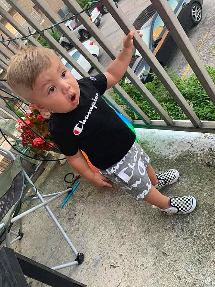 Greyson is registered to the contest to win money with this photo: car, electric_blue, fence, flowerpot, fun, grass, human_leg, knee, leg, leisure, person, plant, recreation, shorts, sitting, sneakers, surprise, t_shirt, thigh, tire