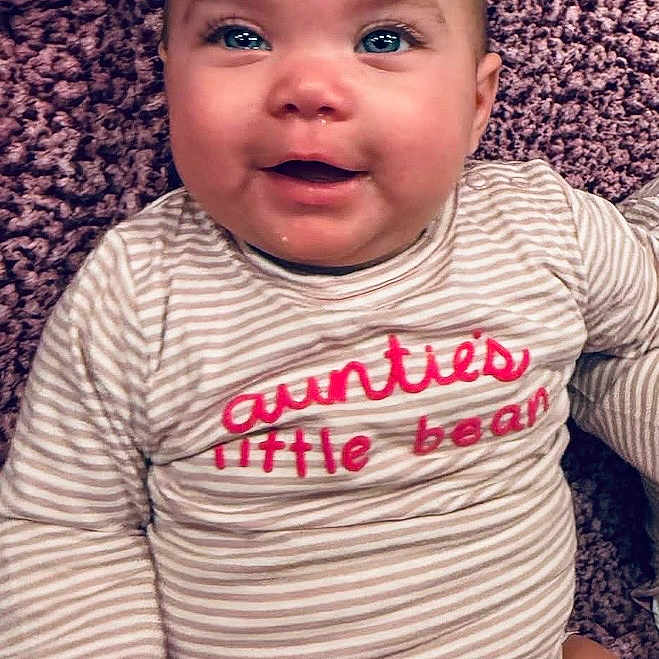 Ezraleigh joined the competition — help win amazing prizes! baby, carpet, child, closeup, cute, eyes, face, happy, head, indoor, infant, onesie, person, portrait, skin, smiling, soft_texture, striped_clothing, text_on_clothing, young