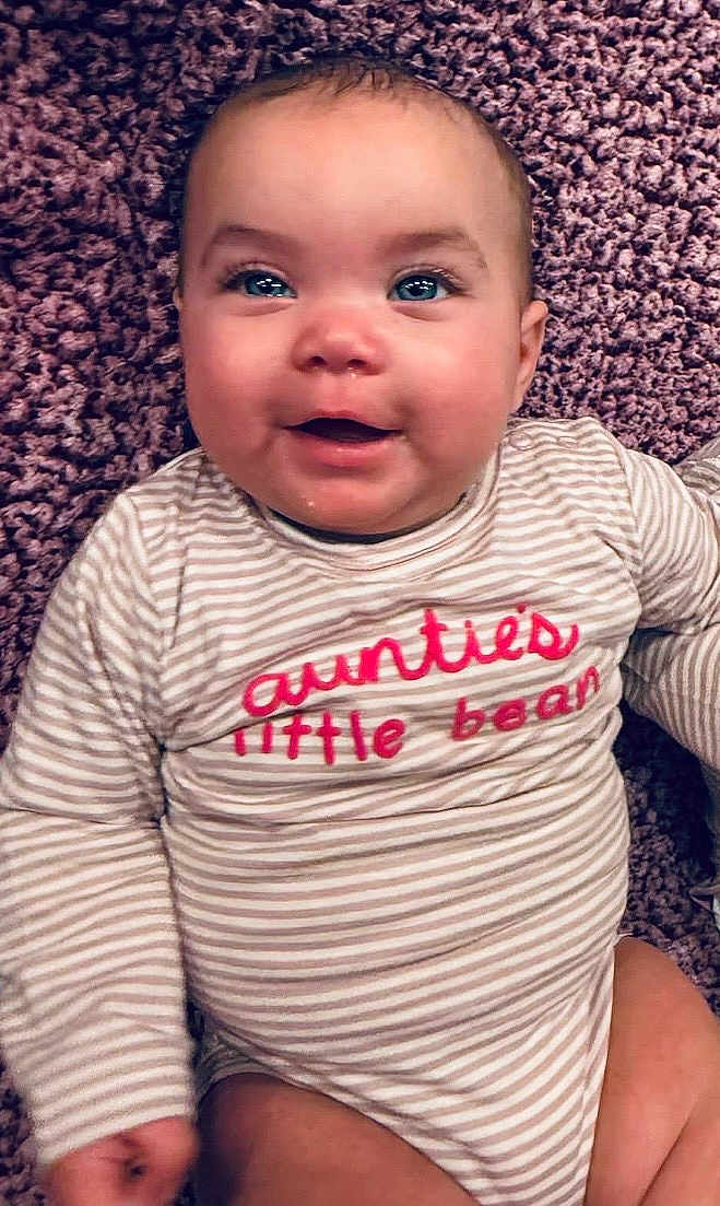 Ezraleigh joined the competition — help win amazing prizes! baby, child, smiling, onesie, striped_clothing, text_on_clothing, face, eyes, happy, infant, person, cute, carpet, soft_texture, indoor, portrait, closeup, skin, head, young