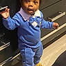Zion is registered to the contest to win money with this photo: child, toddler, blue_outfit, bow_tie, indoor, floor, wooden_floor, standing, curious, expression, small_object, long_sleeves, pants, slippers, black_hair, person, home, cabinet, drawer, light