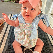 Oaklynn is registered to the contest to win money with this photo: baby, child, smiling, headband, pink_bow, dress, floral_pattern, socks, outdoor, porch, mat, sunlight, happy, cute, infant, blue_ribbons, greenery, sitting, person, face