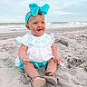 Oaklynn is registered to the contest to win money with this photo: baby, child, beach, sand, ocean, waves, headband, bow, blue, white, clothing, sitting, happy, smiling, outdoor, nature, infant, portrait, footwear, sunset