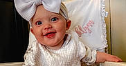 Oaklynn joined the competition — help win amazing prizes! baby, bow_headband, smile, chair, bib, infant, happy, indoor, person, pink_text, pillow, patterned_clothing, headwear, cute, child, skin, foot, hand, wood_floor, white_furniture