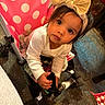 toddler, child, stroller, bow, headband, pink, polka_dot, indoor, floor, clothing, curious, face, hands, person, baby, seat, expression, cute, young, girl