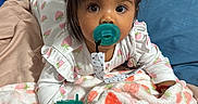Melissa is registered to the contest to win money with this photo: baby, pacifier, blanket, strawberry_pattern, bed, pajamas, infant, face, child, lying_down, indoors, cozy, clothing, person, soft_texture, headband, looking_at_camera, cute, resting, phone