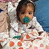 baby, pacifier, blanket, strawberry_pattern, bed, pajamas, infant, face, child, lying_down, indoors, cozy, clothing, person, soft_texture, headband, looking_at_camera, cute, resting, phone