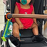 baby, child, stroller, pacifier, red_clothing, headband, toy, indoor, cute, infant, footwear, black_shoes, toddler, seat, curious, person, young_child, plaything, fabric, baby_accessory