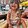 toddler, child, smiling, happy, outdoor, urban, table, wood, umbrella, headband, colorful_clothing, baby, person, sitting, shoes, summer, daylight, street, vehicle, phone