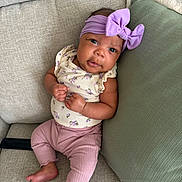 Kehlani is registered to the contest to win money with this photo: baby, infant, headband, bow, couch, pillow, clothing, pink_pants, floral_top, skin, face, eyes, hands, feet, furniture, indoor, cute, child, portrait, relaxing