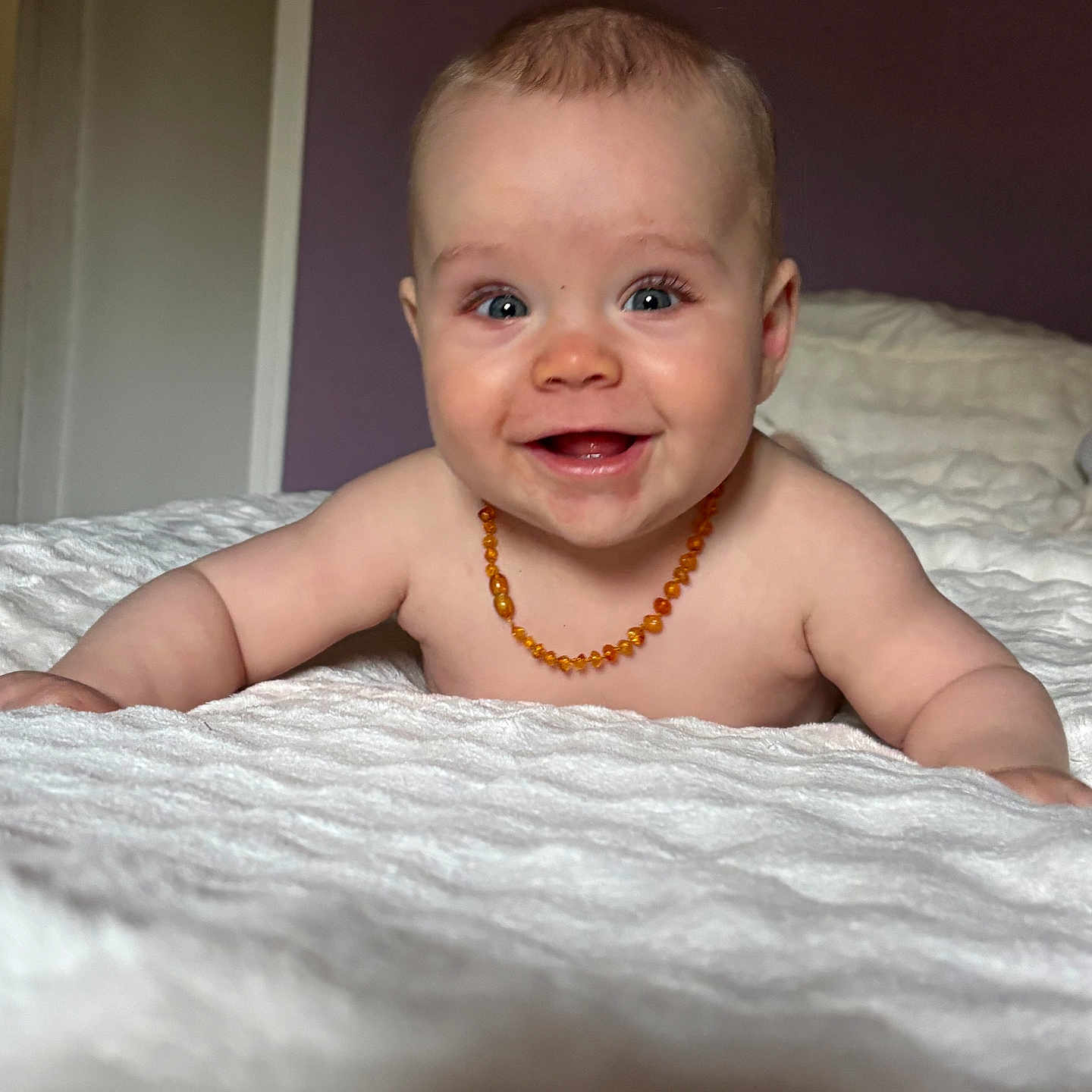 Gabin a rejoint le concours — aidez-le/la à gagner de superbes lots ! baby, smiling, infant, face, necklace, bare_shoulders, white_blanket, bedroom, purple_wall, door, happy, cute, child, portrait, indoor, skin, person, laying, young, toddler