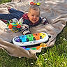 baby, blanket, grass, outdoor, toy, colorful, piano, activity_toy, smiling, child, infant, sunlight, clothing, playtime, happy, nature, greenery, casual, cute, lying_down