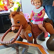 Bella joined the competition — help win amazing prizes! toddler, child, toy_horse, pacifier, indoor, living_room, television, animation, person, adult, pink_clothing, shorts, bib, carpet, glass_table, furniture, happy, smiling, support, play