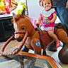 toddler, child, toy_horse, pacifier, indoor, living_room, television, animation, person, adult, pink_clothing, shorts, bib, carpet, glass_table, furniture, happy, smiling, support, play