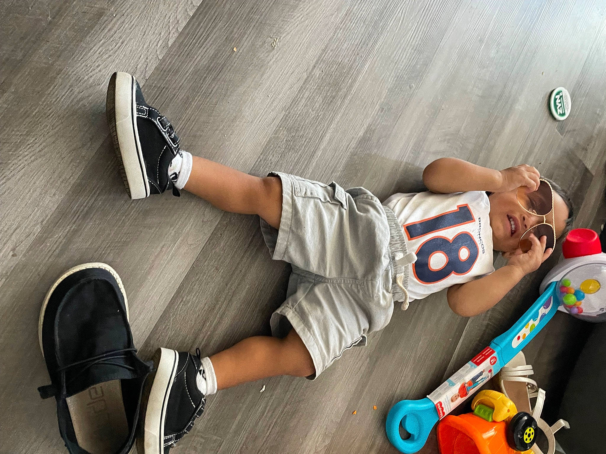 Diego is registered to the contest to win money with this photo: elbow, eyewear, fashion_accessory, font, foot, guitar, human_leg, knee, pattern, person, plaid, sandal, shoe, shorts, sitting, sneakers, sock, sportswear, thigh, toy