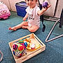 Melody participe au concours pour gagner de l'argent avec cette photo : baby, carpet, child, colorful_toys, disney_toy, expression, face, floor, furniture, indoor, person, playful, purple_toy, ride_on_toy, sitting, smile, toddler, toy, white_onesie, wooden_tray