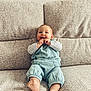 baby, child, infant, couch, sofa, blue_overalls, happy, smiling, barefoot, indoor, person, seated, cozy, cute, fingers, face, foot, comfortable, home, portrait