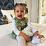 toddler, child, smiling, pigtails, bows, green_dress, white_shirt, white_tights, stuffed_animal, bed, pillow, floral_pattern, indoor, happy, cute, portrait, person, home, cozy, playful