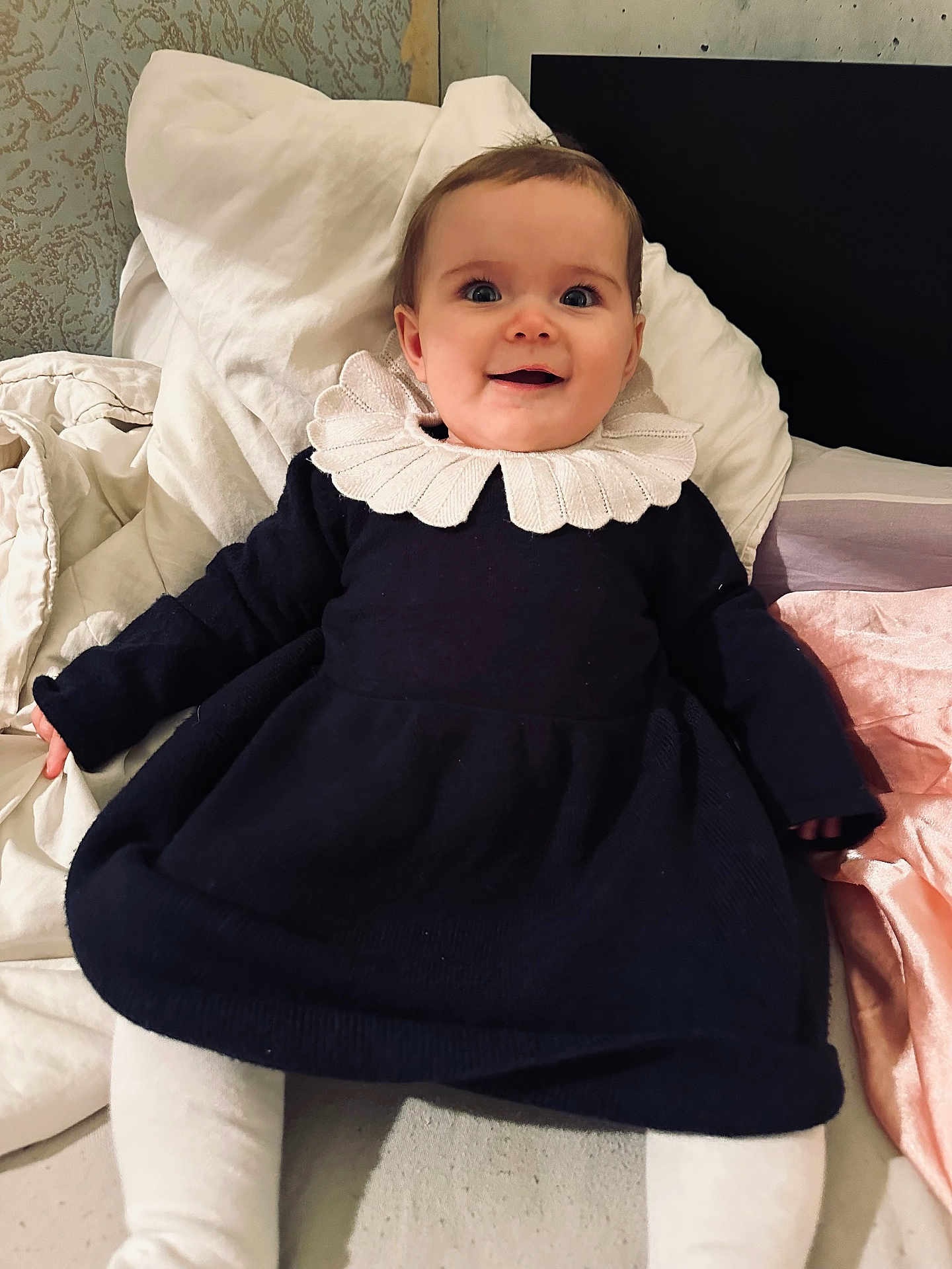 Gabriella a rejoint le concours — aidez-le/la à gagner de superbes lots ! baby, infant, smiling, dress, collar, bed, blanket, white, pink, cozy, happy, child, person, indoor, portrait, cute, young, sitting, textile, fabric