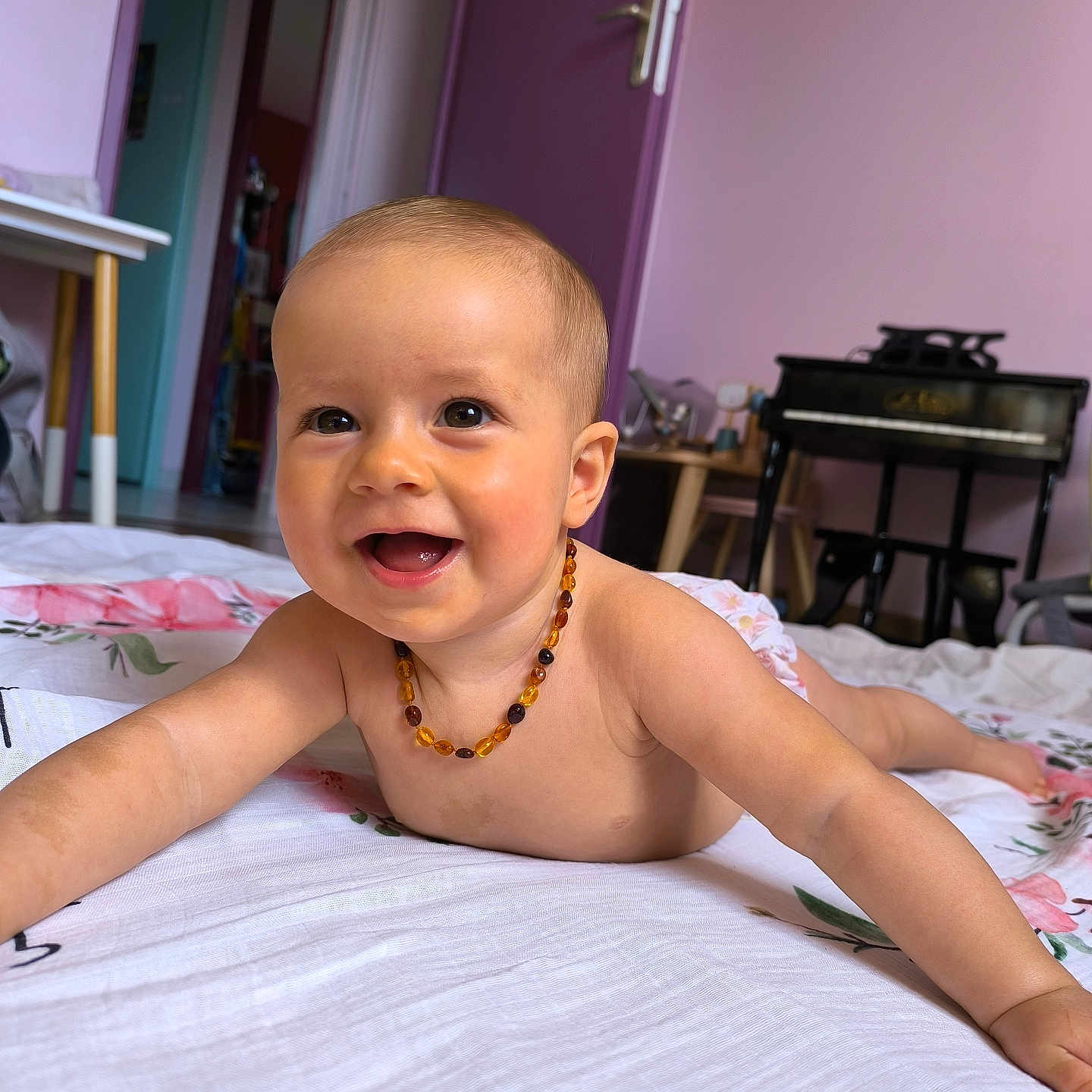 Yüna a rejoint le concours — aidez-le/la à gagner de superbes lots ! amber_necklace, baby, blanket, child, cute, door, floor, floral_pattern, furniture, happy, indoor, infant, lying_down, person, portrait, purple_wall, room, skin, smiling, toy_piano