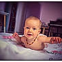 baby, child, smiling, lying_down, blanket, necklace, indoor, face, cute, infant, person, room, furniture, table, chair, soft_light, happy, skin, head, arm