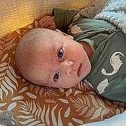 Henry is registered to the contest to win money with this photo: baby, blanket, child, comfort, cozy, cushion, cute, dinosaur_print, face, indoors, infant, looking, lying_down, onesie, patterned, portrait, resting, sleeping_area, soft_texture, young