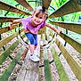 child, girl, playground, wooden_tunnel, forest, trees, greenery, outdoor, smiling, pigtails, purple_shirt, leggings, white_sneakers, play, happy, balance, nature, daylight, fun, adventure