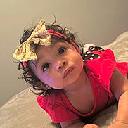Malani is registered to the contest to win money with this photo: adorable, baby, blanket, child, close_up, curly_hair, cute, expression, face, golden_bow, hands, headband, indoor, infant, lying_down, portrait, red_clothing, skin, soft_lighting, young_child