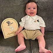 Maverick joined the competition — help win amazing prizes! baby, child, infant, smiling, happy, portrait, sitting, sofa, couch, milestone, three_months, plaque, wooden_sign, barefoot, shorts, shirt, collar, indoor, home, photography