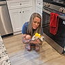 animal, bottle, cabinet, cute, feeding, floor, granite_countertop, home, indoor, kitchen, kitten, love, oven, pet_care, red_towel, sandals, small_pet, tattoo, woman, wood_floor