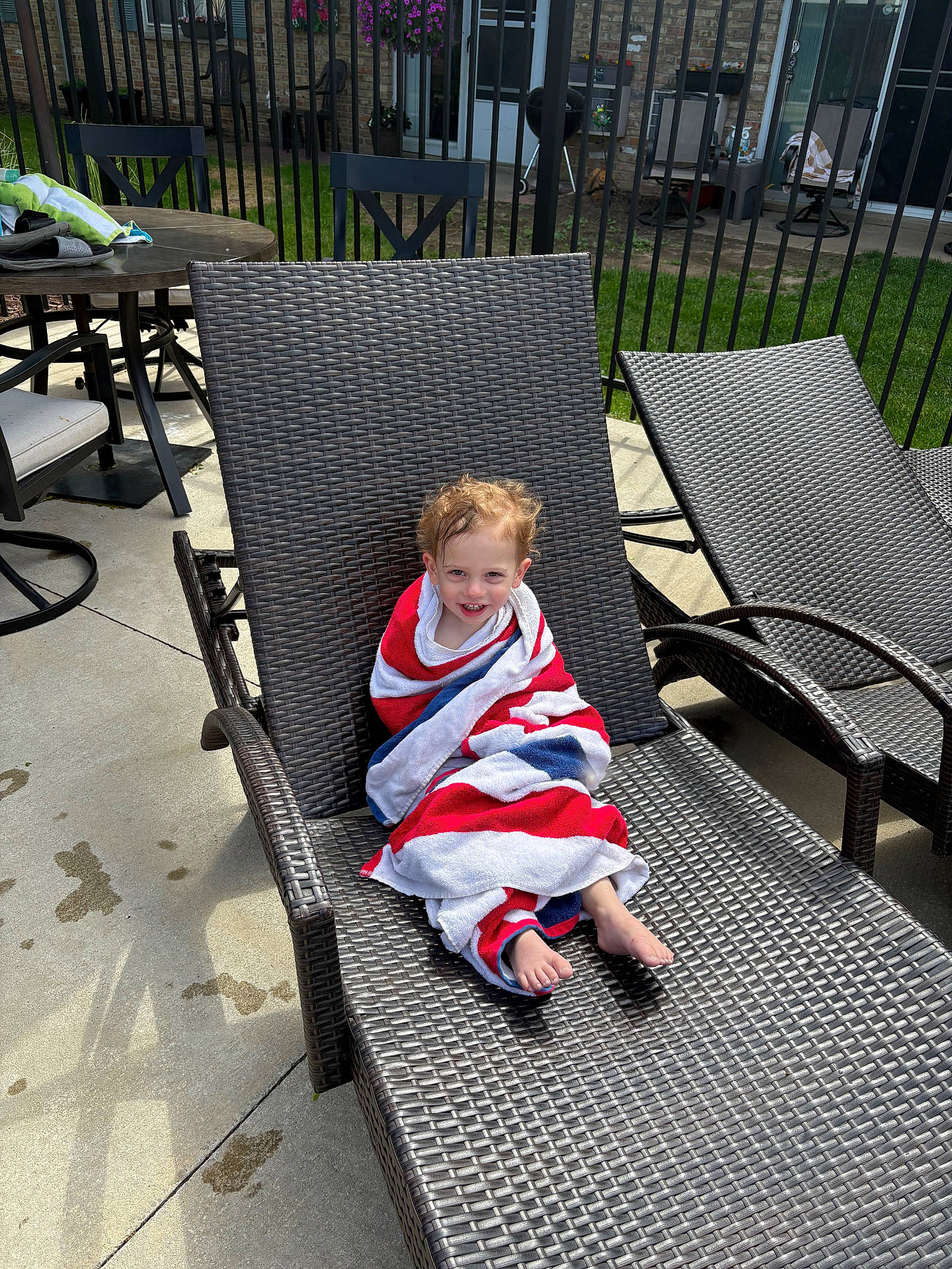 Colin is registered to the contest to win money with this photo: backyard, barefoot, chair, child, concrete, fence, grass, hair, happy, lounge_chair, outdoor, patio, person, relaxing, shadow, smiling, summer, sunlight, table, towel