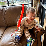 Colin is registered to the contest to win money with this photo: child, balloon, couch, leather, window, shoe, sneaker, indoor, smiling, happy, boy, clothing, urban, daylight, street, sign, casual, cozy, patterned_sweater, toy