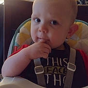 Elijah is registered to the contest to win money with this photo: toddler, child, high_chair, indoor, baby, face, expression, hand, curious, seat, cushion, clothing, home, light, background, person, young_child, eating, chewing, furniture